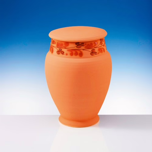 Schweiz. Verband der Bestattungsdienste Eine terrakottafarbene Keramikurne mit einem Deckel und einem einfachen dekorativen Muster im oberen Bereich vor einem Hintergrund mit blauem und weißem Farbverlauf.